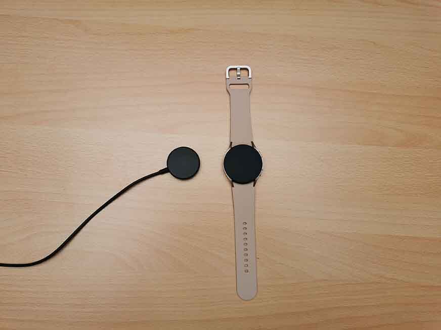 Часы Samsung Galaxy Watch 4 рядом с зарядкой.